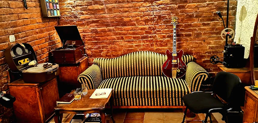 The lounge: striped sofa, a guitar, the gramophone and the tape machine